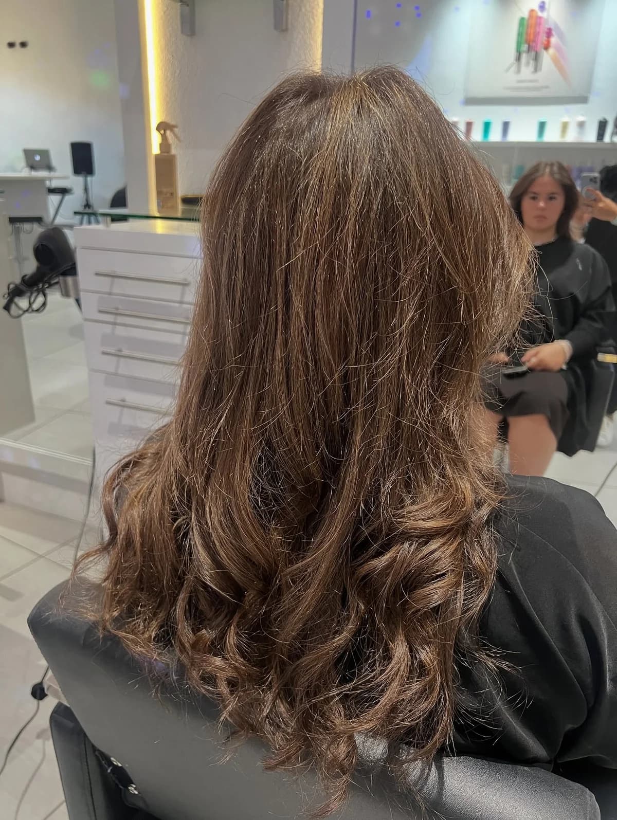 Natural brown balayage with soft waves, viewed from behind in the salon