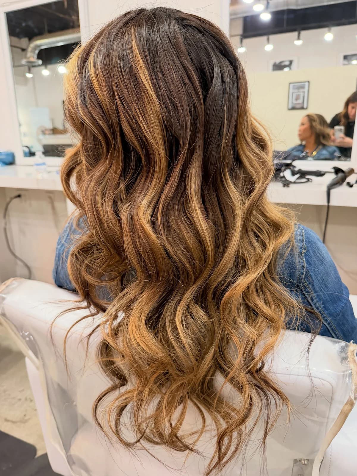 Soft caramel balayage in long waves, viewed from behind in the salon
