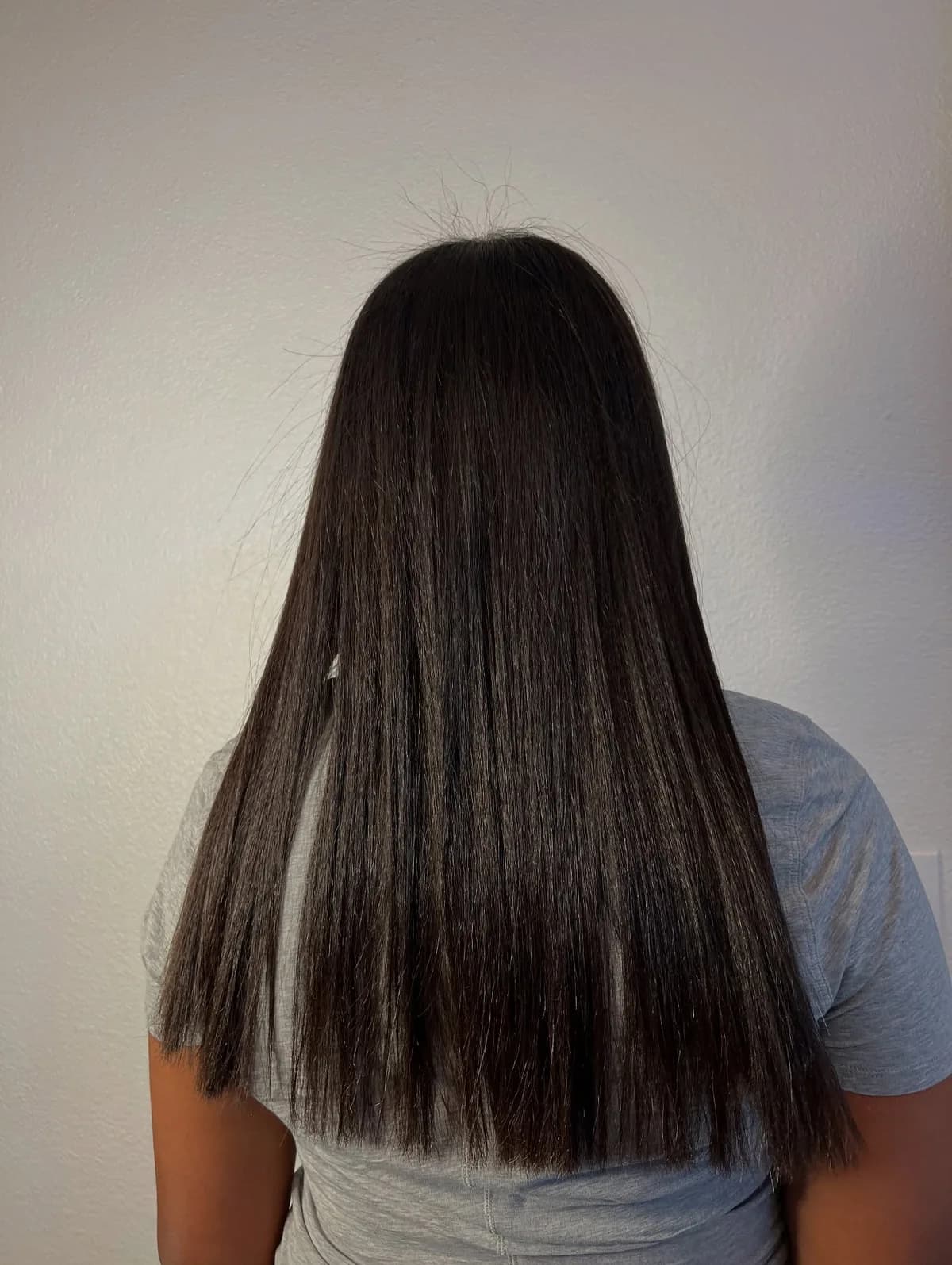 Long straight dark hair on a client wearing a grey shirt, photographed from behind